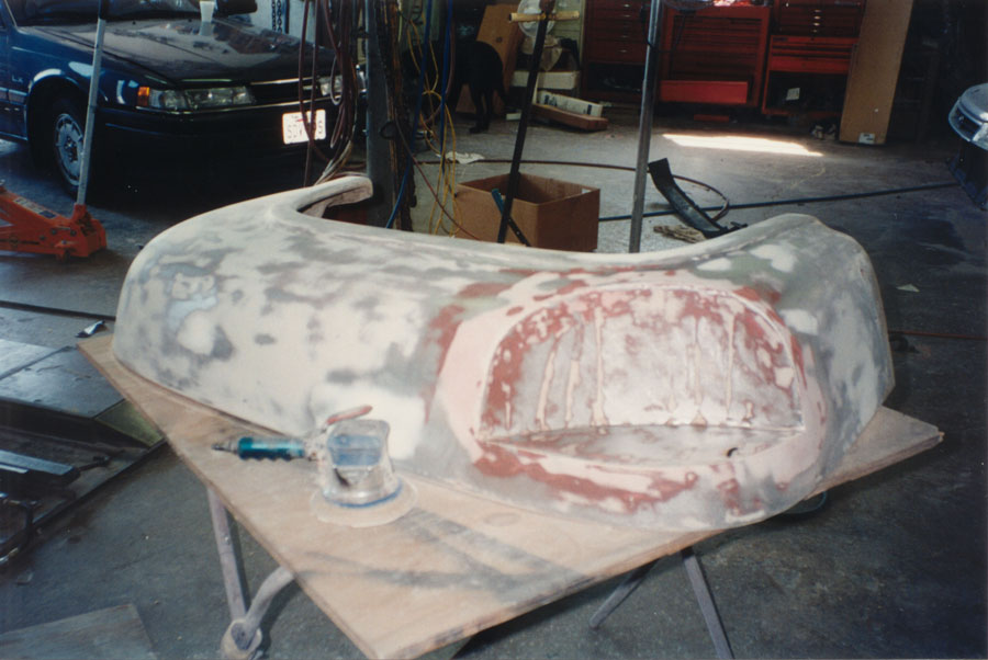 Truck front fender on shop table sanded through primer with pink filler and DA sander