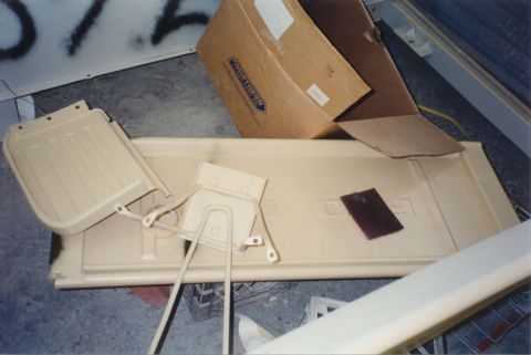 1968 Ford F-100 - A truck tailgate sprayed in tan primer lies face-up on a shop floor with stamped lettering still visible under the primer and a purple sand…