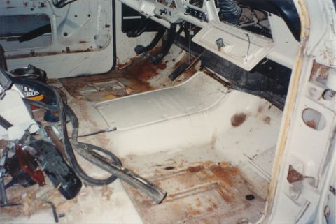 1968 Ford F-100 - Interior of a classic pickup cab stripped to bare metal, showing the white-painted floor pan and transmission tunnel with surface rust arou…