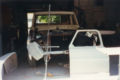 1968 Ford F-100 - Head-on front view of a classic pickup stripped to the cab and frame inside a garage, with the grille, hood, front fenders and both doors r…