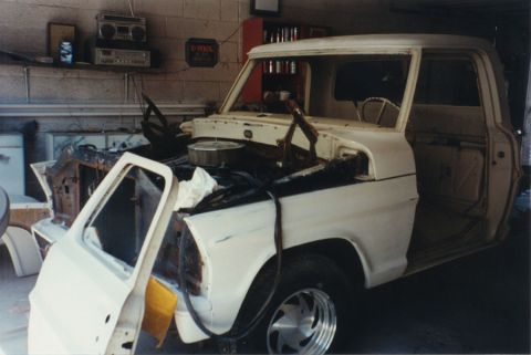 1968 Ford F-100 - Left-front three-quarter view of a white classic pickup mid-teardown in a garage, with the hood, front fender and inner fender apron remove…