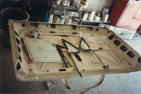1968 Ford F-100 - A truck hood removed from the vehicle and laid underside-up on stands in a body shop, showing the bare primered inner bracing, hinge holes…