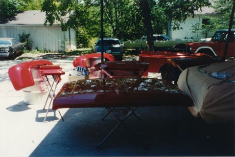 1968 Ford F-100 - Freshly painted red pickup body panels laid out to dry on stands in a driveway, a hood on sawhorses in the foreground with wet gloss reflec…