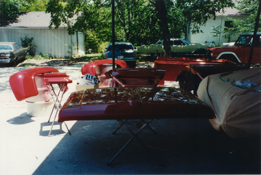 Freshly painted red pickup hood, fenders and bedsides drying on stands in a driveway