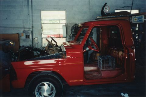 1968 Ford F-100 - Freshly painted bright red classic Ford pickup cab and front clip inside a body shop, with the doors open, no seat or glass installed, and…