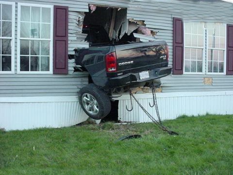 1991 Ford Bronco - A black Dodge Ram truck has crashed through the side of a house, with its rear end protruding from the wall.