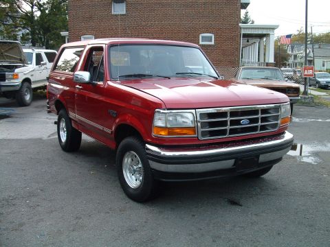 1994 Ford Bronco - A red Ford Bronco is parked next to a white SUV with its hood open.