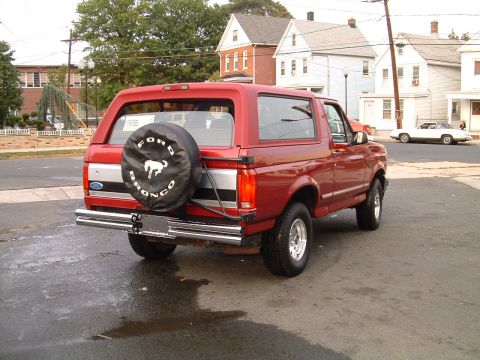 1994 Ford Bronco - Rear view of a red 1994 Ford Bronco, showing the spare tire cover and chrome bumper.