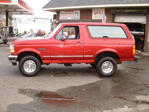 1994 Ford Bronco - This red 1994 Ford Bronco is parked on a wet asphalt lot in front of a repair shop.