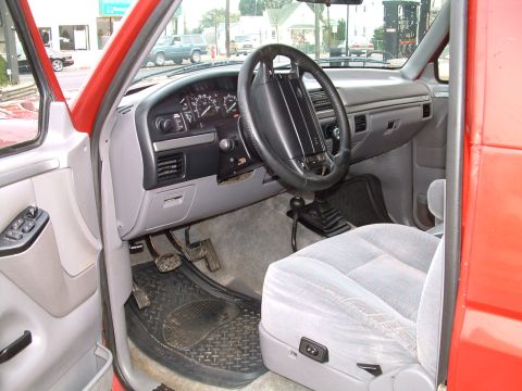1994 Ford Bronco - The interior of a red Ford Bronco, likely from the early 1990s, is shown from the driver's side door.