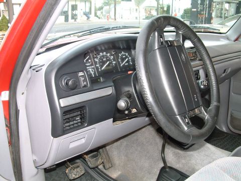 1994 Ford Bronco - Driver's-side dashboard view inside a red Ford truck, showing the analog speedometer and tachometer cluster, leather-wrapped steering wheel…