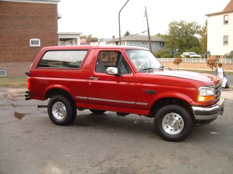 1994 Ford Bronco - Passenger-side three-quarter front view of a red two-door full-size Ford Bronco with removable hardtop, chrome rocker molding and "BRONCO"…