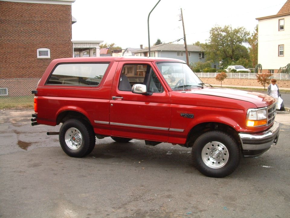 Red two-door Ford Bronco front quarter view on chrome wheels parked on a residential street