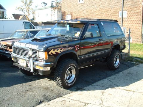 1994 Ford Bronco - This modified SUV features flame decals on the fender and a prominent hood scoop, parked next to another vehicle.