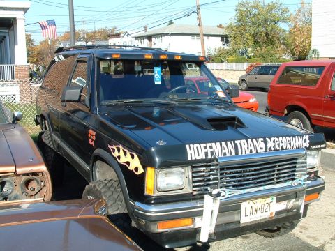 1994 Ford Bronco - This black SUV has flame decals and custom text on the hood, parked next to other vehicles.
