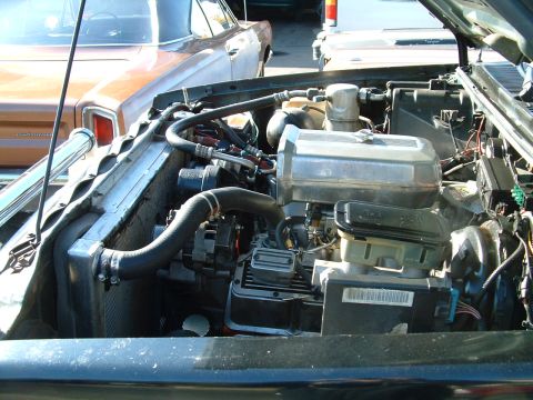 1994 Ford Bronco - Engine bay details with radiator and hoses visible, alongside a background vehicle.