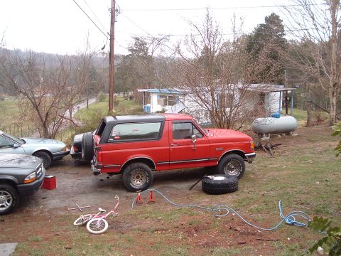 1987 Ford Bronco - A red 1987 Ford Bronco with a black top is parked outdoors, with a spare tire and jack nearby.