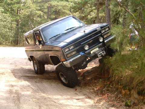1994 Ford Bronco - This off-road vehicle is navigating a steep dirt incline with trees on the right.
