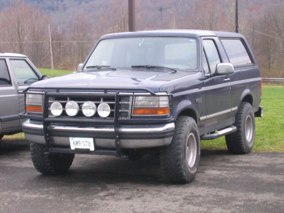 Dark blue Ford Bronco with brush guard and off-road lights parked on pavement