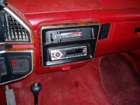 1990 Ford Bronco - The interior of a vehicle shows a red dashboard with a gear shift and two radio units installed.
