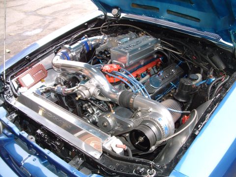 1988 Ford Mustang - The engine bay of a blue 1988 Ford Mustang is visible, a supercharger and custom modifications.