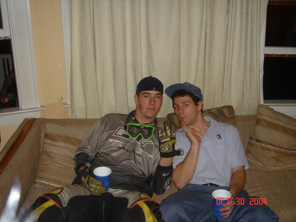 Two young men in motocross gear sitting on a couch with red cups