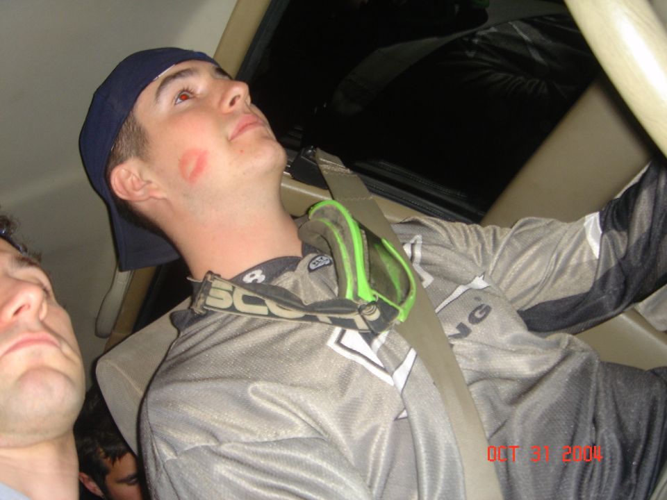 Man with a kiss mark on his cheek wearing goggles and a racing jersey inside a vehicle