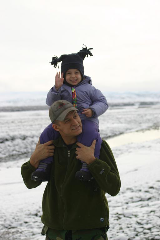 Dad gives kid a piggyback ride in the snow. Kid waves