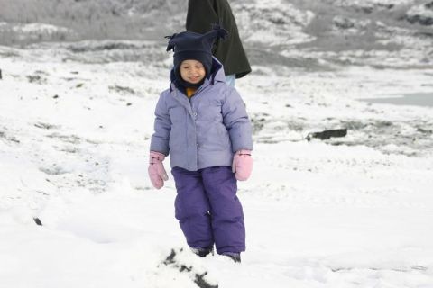 1985 Ford Bronco - A child dressed for winter walks through a snowy landscape, with a dark figure in the background.