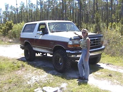 1993 Ford Bronco - A woman poses with a lifted two-tone Ford Bronco in a wooded area.