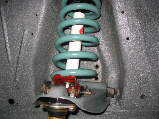 Green coil spring and white shock installed in gray Mustang shock tower with red perch and new hardware