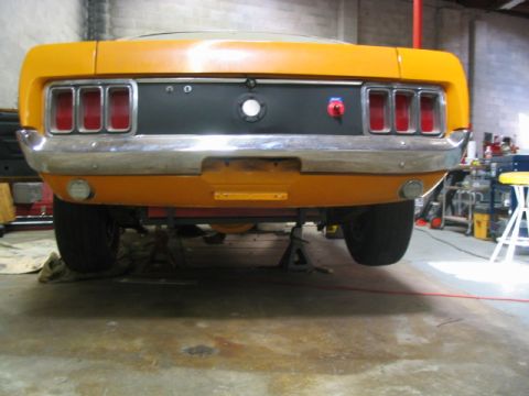 1970 Ford Mustang - Rear view of a yellow 1969 Ford Mustang undergoing work, supported by jack stands in a garage.