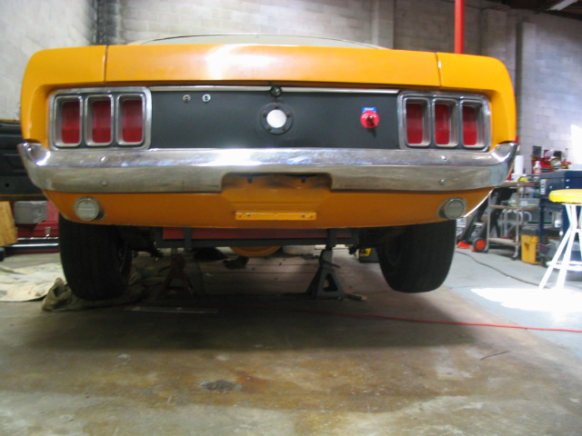Rear view of orange classic Mustang on jack stands in a shop, tri-bar taillights