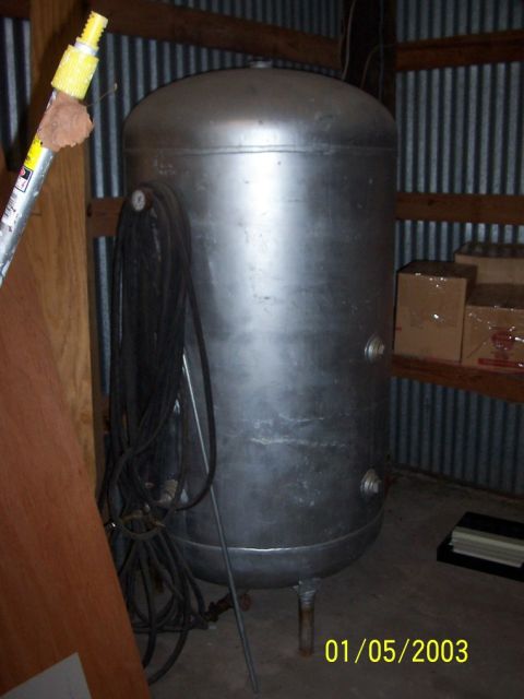 1979 Ford Bronco - A large, cylindrical air compressor tank is shown indoors, with a coiled black hose hanging from its side and a pressure gauge visible.