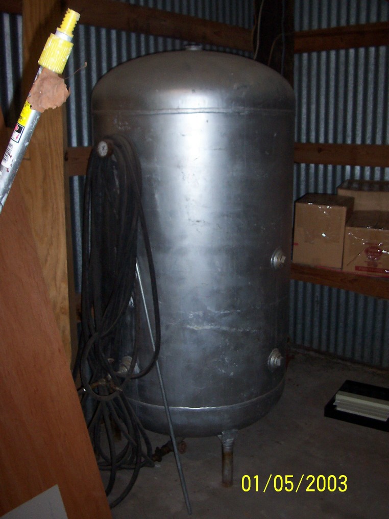 Large silver air compressor tank with coiled hose and pressure gauge