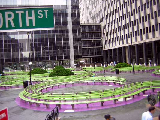 Green sign reading "NORTH ST" above a park with curved green benches