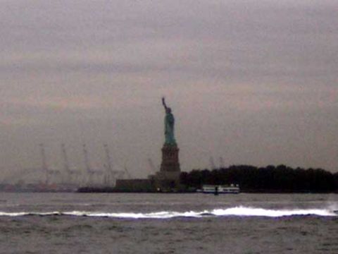 1995 Ford Bronco - The Statue of Liberty stands tall against a cloudy sky, with a ferry boat and industrial cranes visible in the distance.