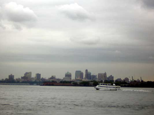 White ferry boat moving on water with a city skyline in the background under a cloudy sky