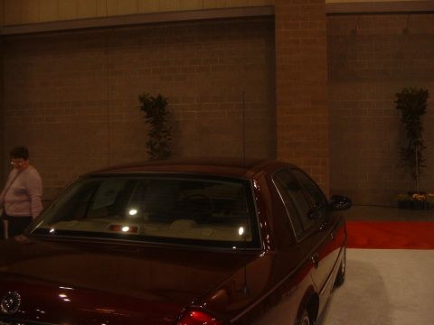 1999 Ford Crown Victoria - A dark red sedan is displayed indoors with a brick wall backdrop and a red carpet.
