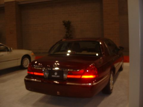 1999 Ford Crown Victoria - A red Mercury Grand Marquis is seen from the rear at an auto show, with a white car partially visible to the left.