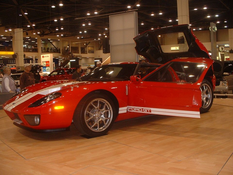 Red Ford GT supercar with white stripes and open door at an indoor auto show