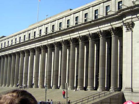 1995 Ford Bronco - A large building with classical architecture and a row of columns stands under a bright blue sky.