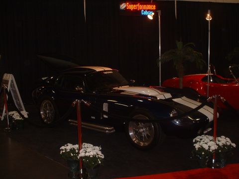 1999 Ford Crown Victoria - A dark blue coupe with white racing stripes is displayed indoors next to a red car.