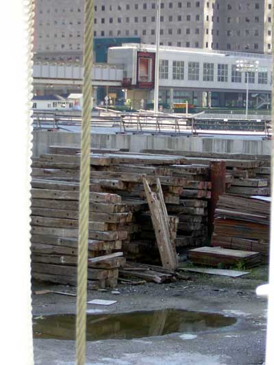 1995 Ford Bronco - A construction site scene with piles of lumber and a reflective puddle, set against a backdrop of urban buildings.