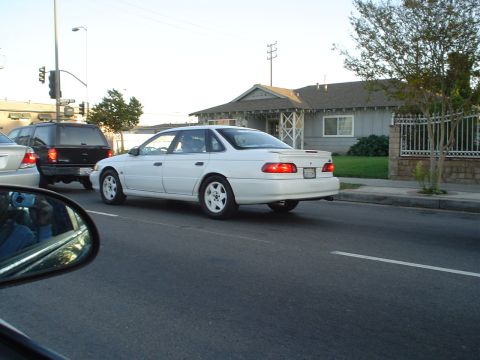 1993 Ford Taurus - A white 1993 Ford Taurus sedan is seen from the rear, driving on a street.