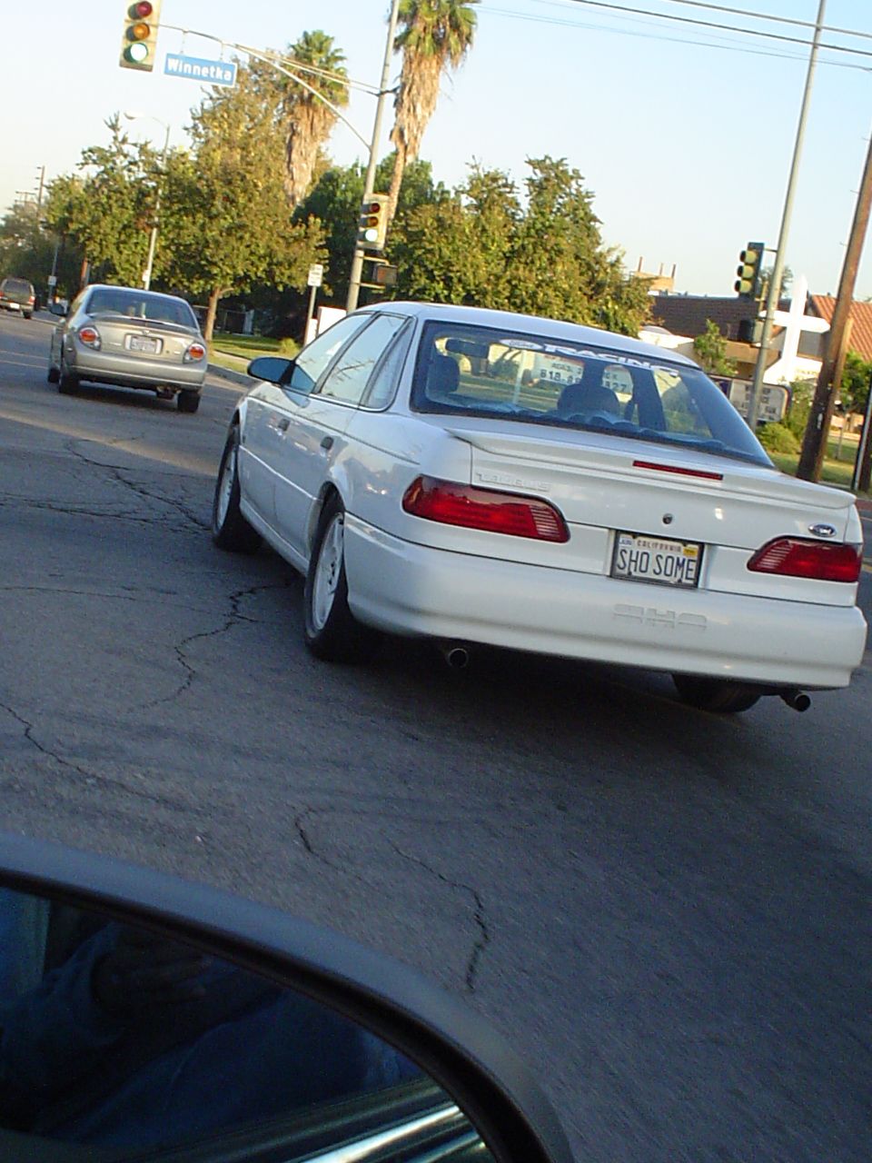 White 1993 Ford Taurus SHO with custom license plate 'SHO SOME' driving on a street. Another car is visible ahead