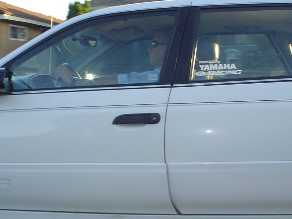 Driver in white sedan with Yamaha Racing window sticker, side view