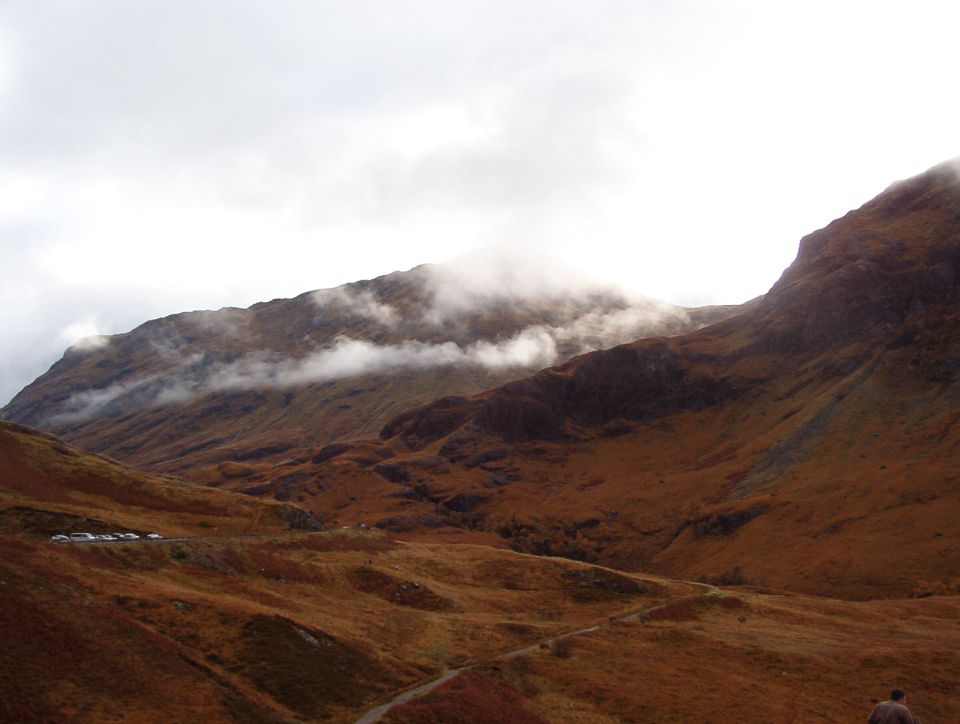 Misty highland glen with russet slopes and a distant road with parked cars