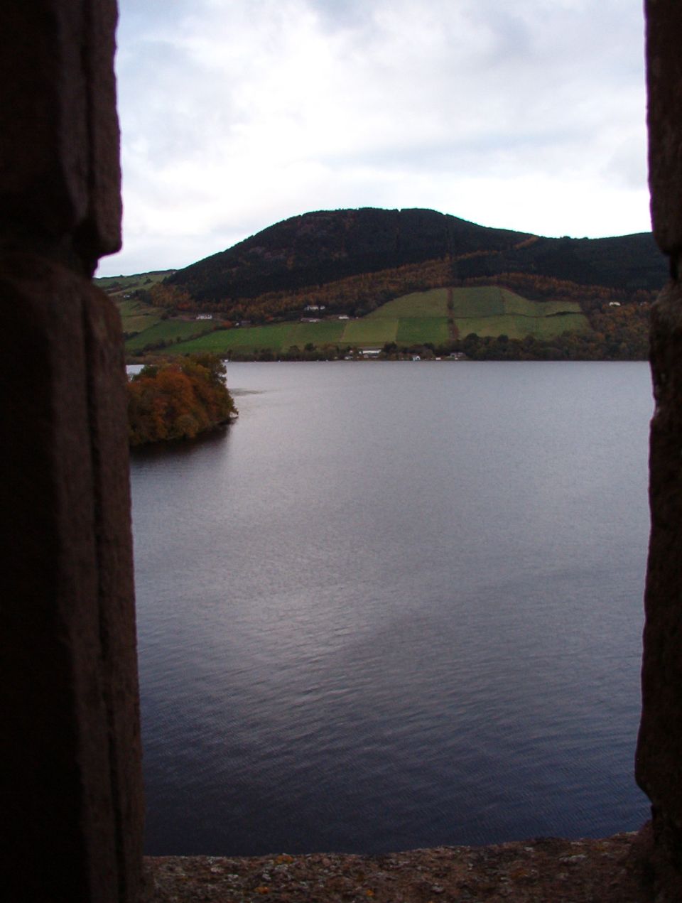Loch Ness and a forested hillside framed by a stone castle window opening
