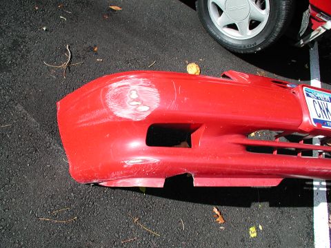 1992 Ford Taurus - Damaged red car bumper resting on asphalt, with a partial wheel in the background.